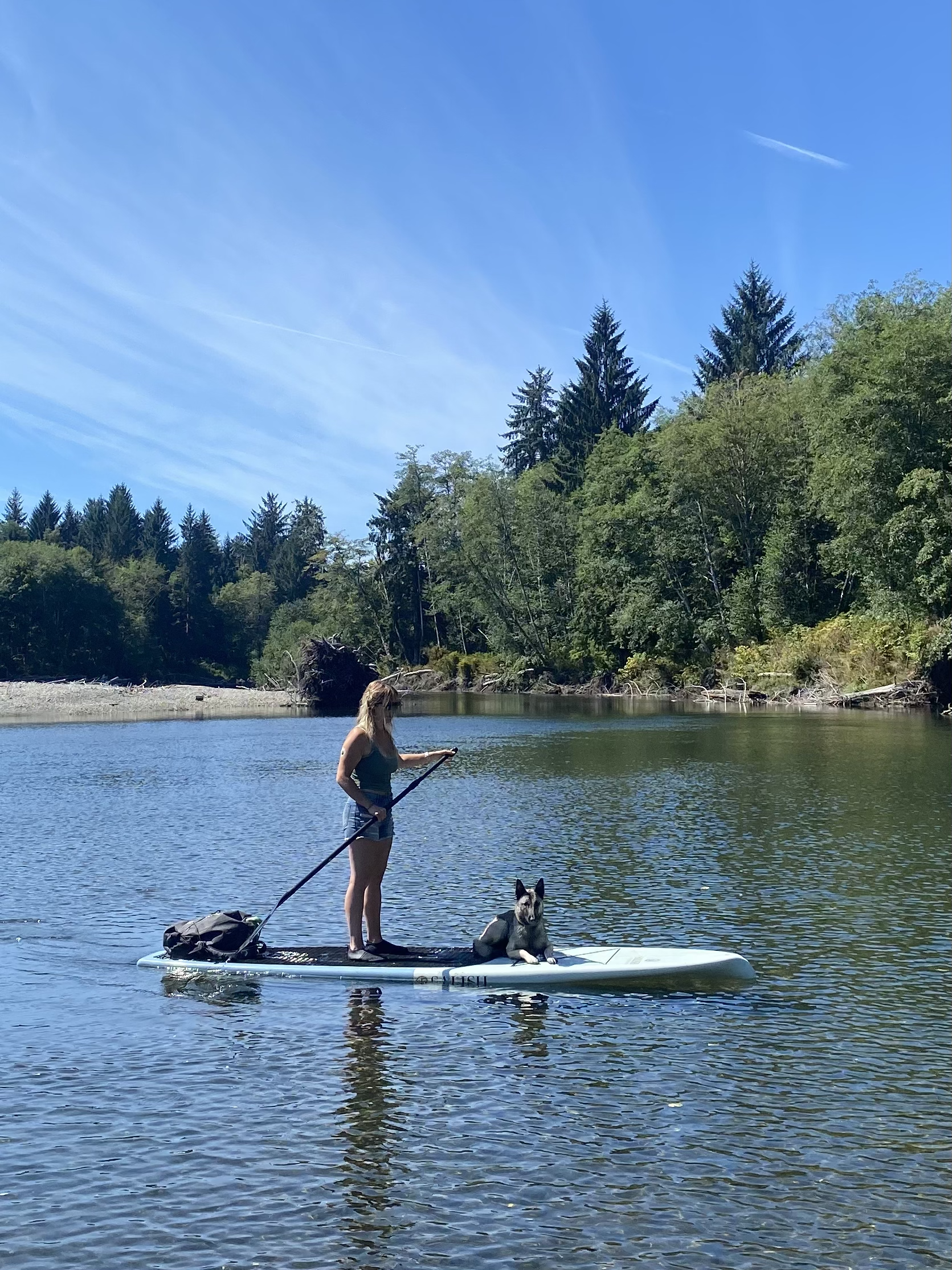 Chelsea paddleboarding on calm river water in Port Renfrew with forest backdrop